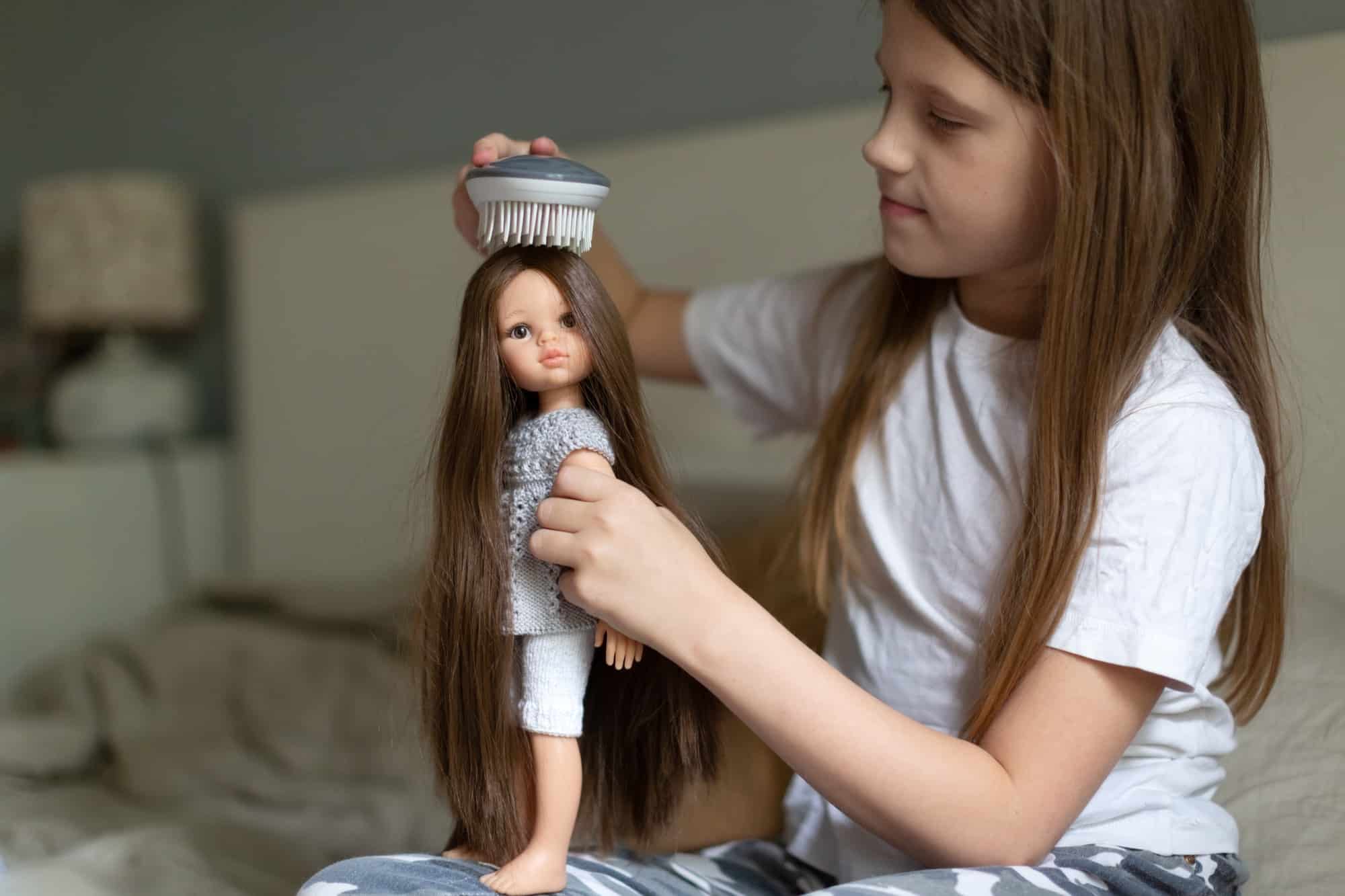Caucasian girl combing a doll with long hair, a girl playing dolls. Traditional children's games