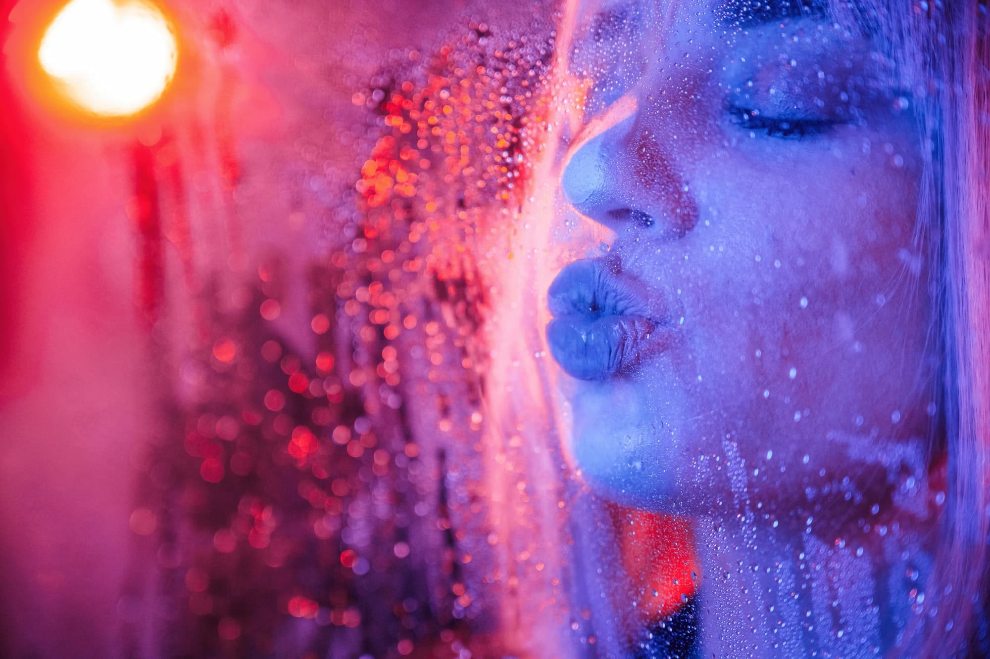 Kissing the surface. Stylish woman with white hair is behind wet transparent plastic sheet